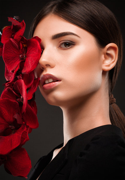 迷人的女孩肖像，健康干净的皮肤和美丽的化妆。美学美容和化妆概念。她手里拿着一朵红花。图片下载