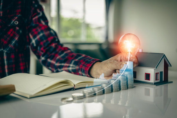 商人手里拿着灯泡，桌上堆着一堆硬币，节能理财观念，办公会计观念。特写照片图片下载