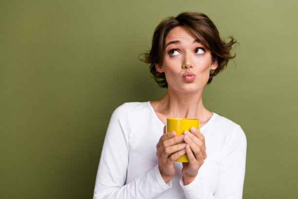 可爱的年轻女士的照片肖像拿着杯子噘起嘴唇看起来空的空间穿着时尚的白色服装孤立在卡其色背景图片下载