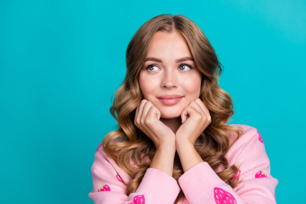 年轻少女模特的照片肖像穿粉红色时髦的套头衫触摸脸颊看起来新奇的白日梦孤立的蓝色背景图片下载