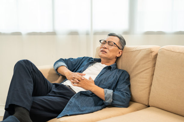 老老头有胃痛和胃炎。成熟的男人把手放在肚子上，挤一挤，放松和安抚，上厕所需要大便。坐在家里客厅的沙发上图片下载