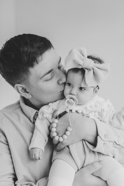在背景墙上，爸爸亲吻小女孩的照片中，他的弓被隔离了。可爱的宝宝在爸爸怀里的特写。爸爸手里抱着6个月大的小女孩。父亲拥抱他的女儿。黑白照片图片下载