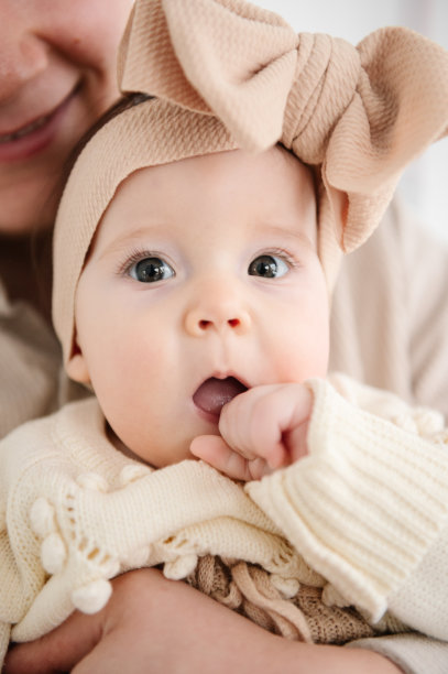 一个可爱的小女孩的肖像，头发扎着蝴蝶结，和爸爸在家里。一个漂亮的小女孩，长着一双大眼睛，头上戴着一个大大的蝴蝶结发带。可爱的婴儿，6个月大，在爸爸的怀里特写。图片下载