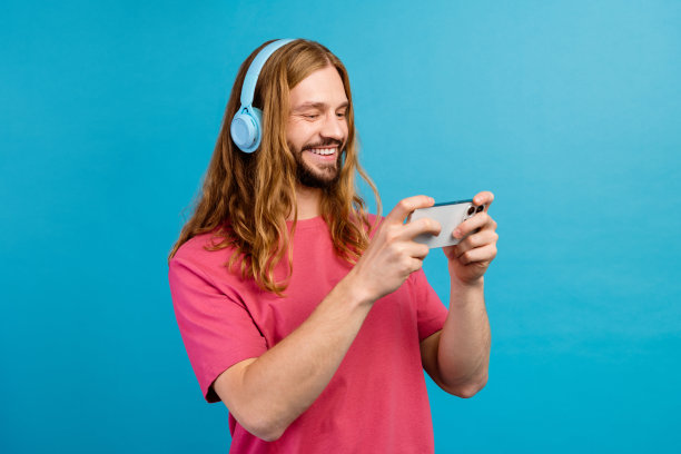 积极的人的个人资料照片，听音乐，耳机，玩游戏，智能手机孤立的蓝色背景图片下载