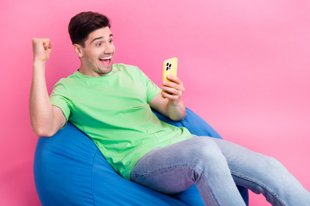 照片的年轻喜出望外的赢家家伙穿着绿色t恤看足球比赛智能手机体育博彩孤立在粉红色的背景图片下载