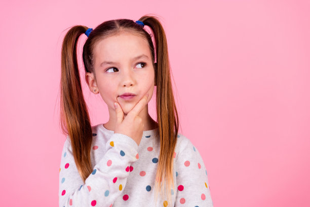 照片中聪明聪明的小女孩梳着尾巴发型，穿着时尚的运动衫，在粉红色的背景下看起来很空旷图片下载