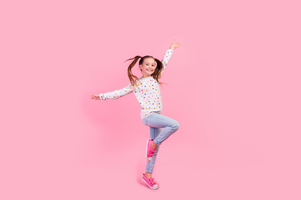 满意的小女孩的全身照片穿着时尚的运动衫牛仔裤举起双手踮起脚尖孤立在粉红色的背景图片下载