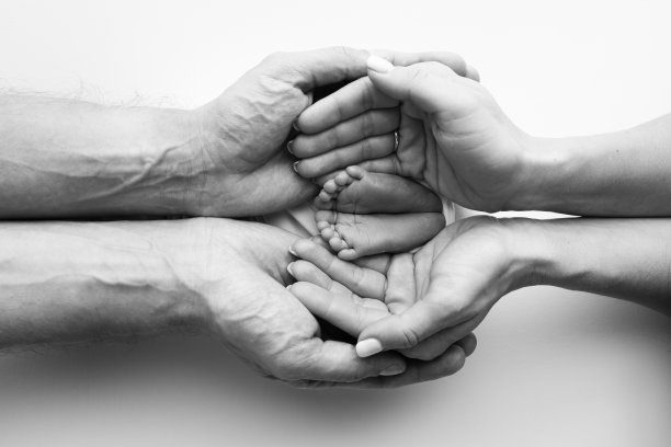 爸爸的手掌，妈妈都抱着刚出生的婴儿的脚。新生儿的脚放在父母的手掌上。工作室微距黑白照片的一个孩子的脚趾，脚跟和脚。图片下载