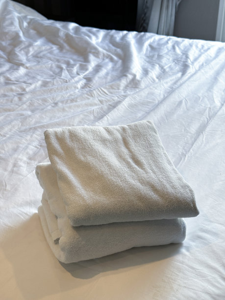 特写图片:白色的酒店毛巾堆在白色的羽绒被床上，折叠的浴巾和手巾放在床垫上，抬高的视角，聚焦于前景图片下载