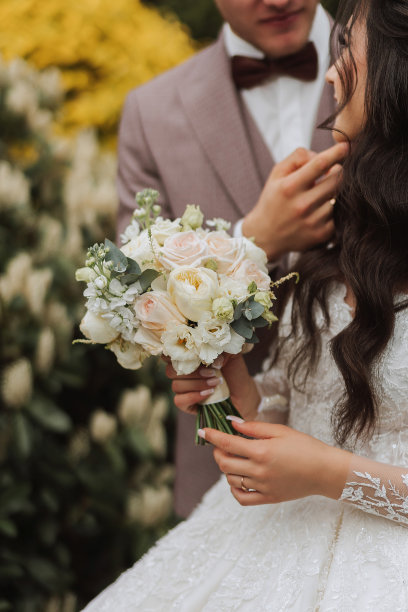 新郎从背后拥抱新娘，新娘手持婚礼花束。裁剪照片。新郎穿黑色西装。细节图片下载