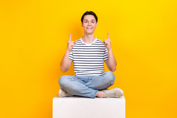 照片中，穿着条纹t恤的清凉开朗的男子用两根手指指着空的空间，孤立的黄色背景图片下载