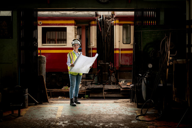 穿着安全背心和安全帽的铁路技术工人在火车维修站按图纸工作的照片图片下载