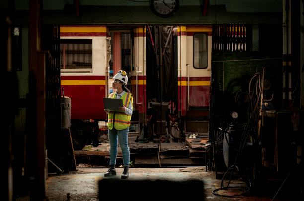 穿着安全背心和安全帽的铁路技术工人在火车维修站按图纸工作的照片图片下载