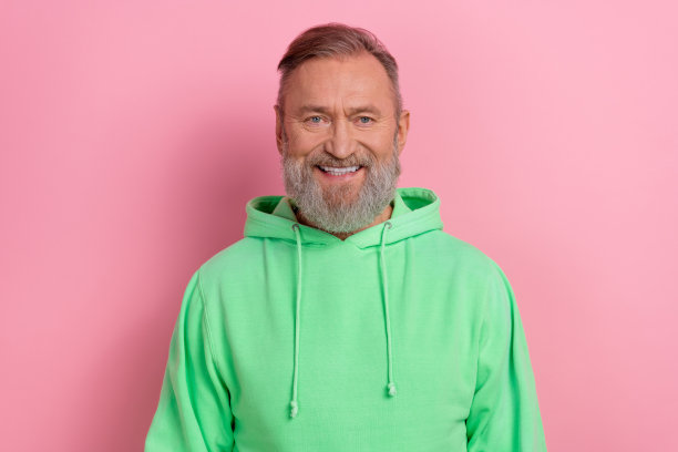 照片中心情愉快的小伙子穿着绿色卫衣微笑着洁白的牙齿孤立的粉红色背景图片下载