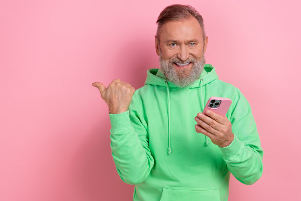 照片正面可爱的家伙穿着绿色卫衣发短信现代设备指向空白的空间孤立的粉红色背景图片下载