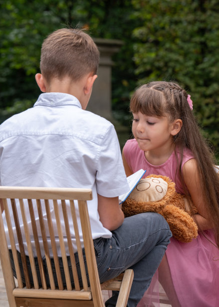 那个男孩背靠在椅子上看书。这个女孩很感兴趣地看了看，想看看照片。6岁的女孩，抱着一只泰迪熊，留着长长的黑发图片下载