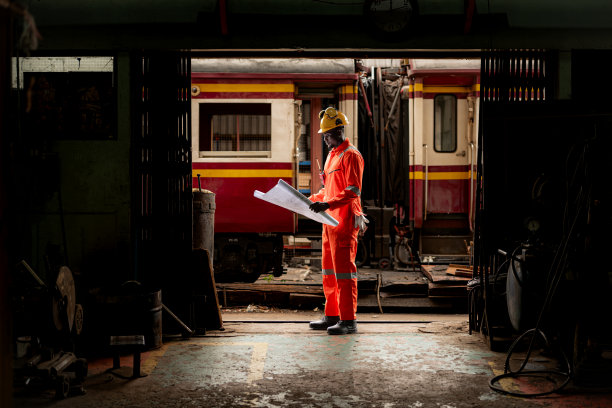 穿着安全背心和安全帽的铁路技术工人在火车维修站按图纸工作的照片图片下载