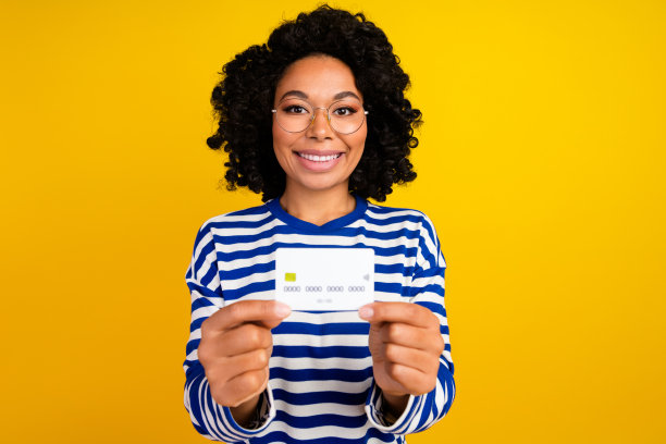 照片中，一个长着牙齿、笑容灿烂的聪明女人，戴着眼镜的手指上戴着chevelure，信用卡被隔离在明亮的黄色背景上图片下载