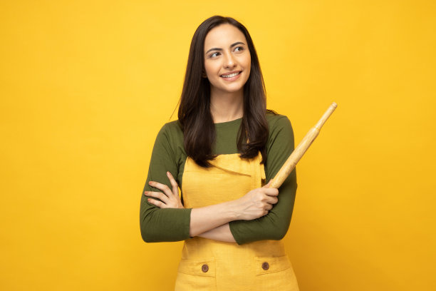 印度女厨师戴着围裙，拿着木制擀面杖，孤立地站在黄色背景照片上图片下载