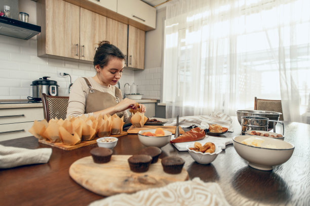 一位年轻女子用手工包装纸杯蛋糕。外卖的概念。一个生日包裹。小生意。面包房厨师在厨房里烘焙糕点和蛋糕，复印空间图片下载