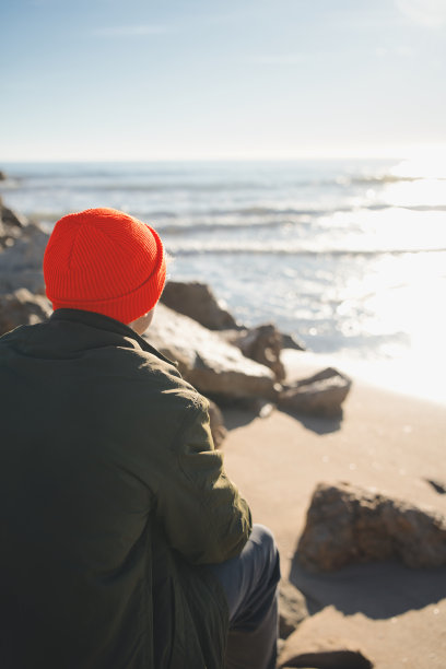竖版照片：年轻男子在海滩日出时看海，背影图片下载