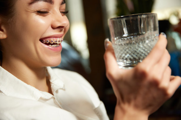 照片中的年轻女子戴着牙套微笑着喝水。补水对口腔健康的重要性。图片下载