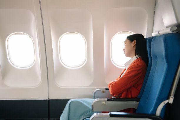 一位沮丧的女士坐在飞机上，双手抱头的照片。一位亚洲女士坐在座位上图片下载