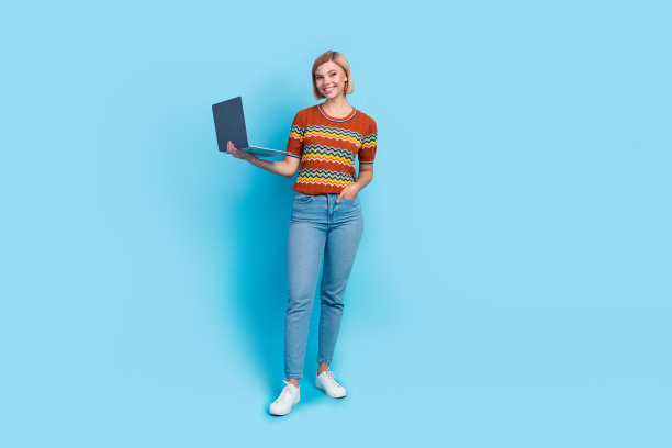 全尺寸照片聪明华丽的女孩穿条纹t恤牛仔裤拿笔记本电脑手臂在口袋里孤立的蓝色背景图片下载