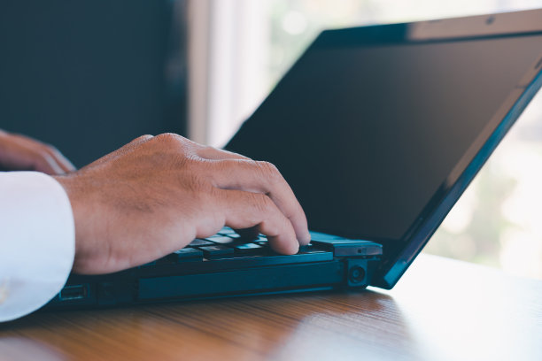 在一张特写照片中，一位商人手里拿着笔记本电脑，他的手机正在桌子上的笔记本电脑上工作。图片下载