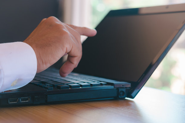 一个商人拿着记事本、笔和电话在桌上的笔记本电脑上工作的特写照片。图片下载