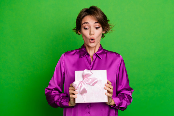 照片迷人有趣的棕色鲍勃头发女孩穿粉红色的衬衫收到额外的奖金礼盒在商店惊讶孤立的绿色背景图片下载
