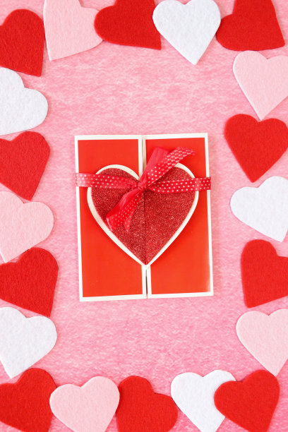 情人节设计海报框架的特写图片，由红色、粉色、白色相间的心形图案围绕着自制的情人节卡片，斑驳的粉色背景，抬高的视角，情人节和浪漫的概念图片下载