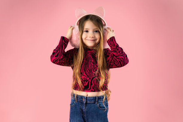 可爱的小女孩戴着粉红色背景的时尚耳罩图片下载