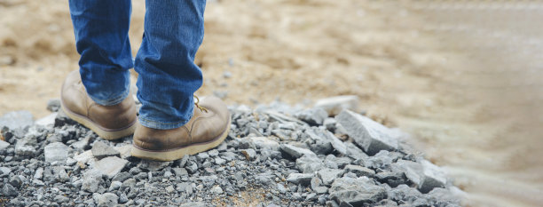 穿着牛仔裤和皮靴的孤独男人的腿沿着布满岩石的小路走着。旅游概念——横幅图片。图片下载