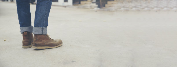 穿着牛仔裤和皮靴的孤独男人的腿沿着布满岩石的小路走着。旅游概念——横幅图片。图片下载