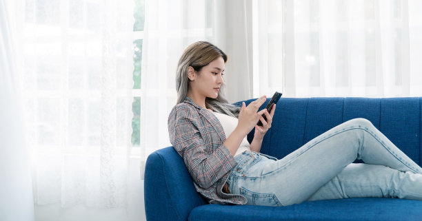 年轻美丽的亚洲女人的肖像放松地使用智能手机小工具在沙发上。微笑快乐的亚洲女孩网购工作在家。教育电子商务自由科技中小企业连接亚洲人图片下载