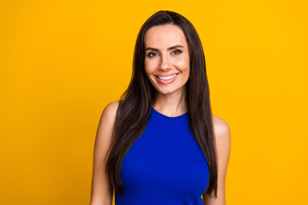 照片中漂亮甜美的女人穿着蓝色上衣，露出白色的牙齿，孤立的黄色背景图片下载