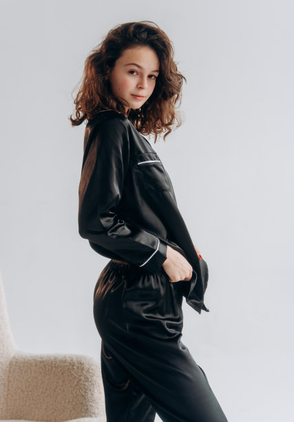 美丽卷曲的女人带着微笑，穿着黑色时尚的睡衣，白色背景图片下载