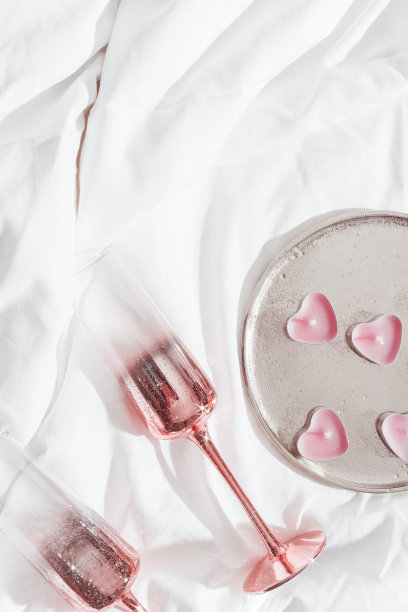 闪亮的粉色香槟酒杯和燃烧着的蜡烛就像床单上的心形。生活美学照片，明星滤镜。情人节，爱情概念，浪漫相遇。酒杯里的起泡酒。图片下载