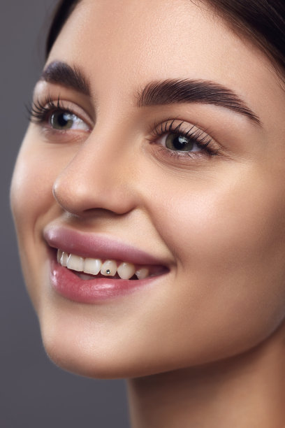 特写女模特的脸，完美的嘴唇和眼妆微笑着看着灰色的工作室背景。图片下载