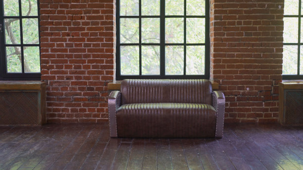 褐色砖墙与皮革沙发。背景照片与文字的复制空间。酒红色皮沙发通往阁楼，室内有明亮的探照灯和一扇窗户。砖墙。砖砌阁楼里的皮沙发。图片下载