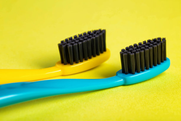 黄色背景上涂有碳涂层的现代牙刷(特写)。中等硬毛的牙刷。口腔护理卫生，宏观图片下载