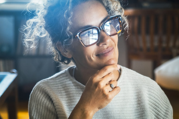 自信迷人的成年女性独自在家思考和做梦的正面照片。积极的态度和生活方式的人的观念。一位女士戴着眼镜，摸着下巴微笑着。空想家图片下载