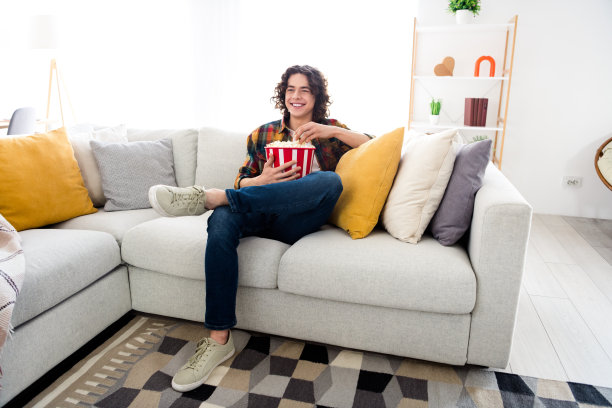 心情好时髦的家伙穿着格子衬衫享受爆米花在室内看电视的家庭房间的全长照片图片下载