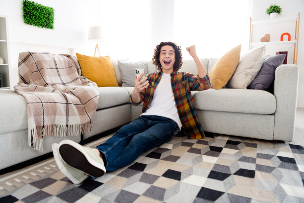 心情好幸运的家伙穿着格子衬衫赢得游戏的全身照片在室内的房子的家庭房间的现代小工具图片下载