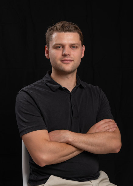 一个穿着黑色t恤的年轻人在黑色背景上的肖像。那人坐在一张白色的椅子上，双臂交叉在胸前图片下载