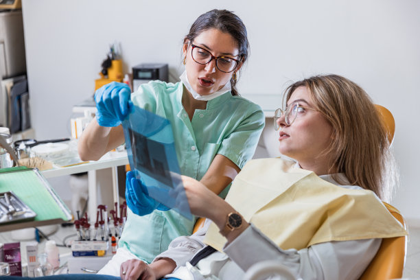 年轻的女牙医向病人展示全景牙科x光片-库存照片图片下载