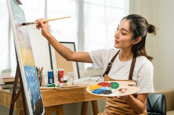 亚洲女艺术家正在用画笔和不同的丙烯酸颜料作画。作为艺术概念的女艺术家在创作工作室的画布上作画图片下载