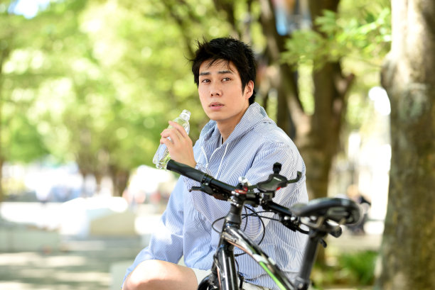 一位年轻的亚洲男子下了自行车，一边休息一边补充水分。图片下载