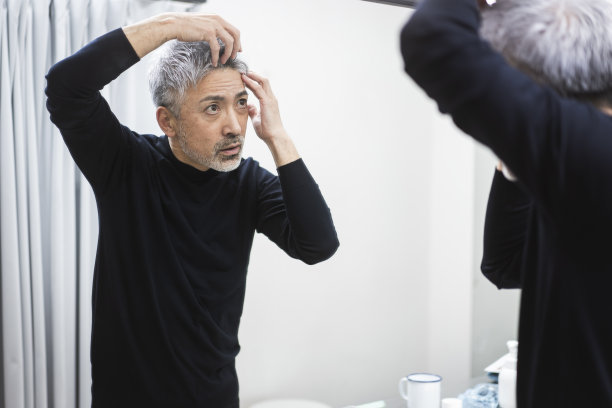 一个男人在照镜子的时候摸着自己的头发。图片下载